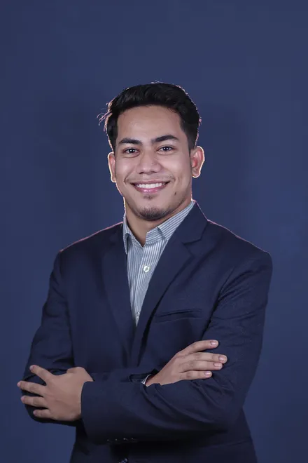 Portrait of Miraj in a navy suit, smiling with arms crossed